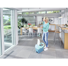 Frau wischt mit einem Mopp und Eimer in einem hellen Raum den Boden.