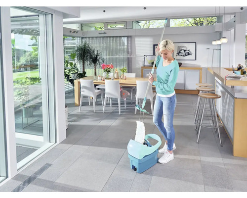 Frau wischt mit einem Mopp und Eimer in einem hellen Raum den Boden.