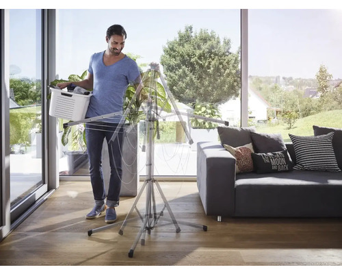 Mann mit Wäschekorb beim Aufstellen eines Wäscheständers in einem hellen Wohnraum.