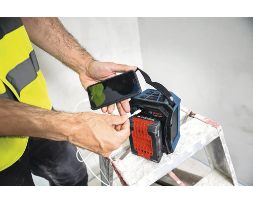 Person lädt ein Mobiltelefon an einem Bosch Baustellenradio auf.