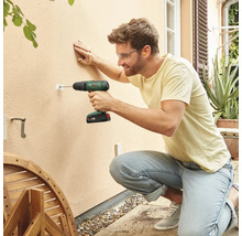 Mann bohrt mit einem Akku-Bohrschrauber ein Loch in eine Wand im Außenbereich.
