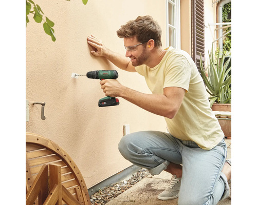 Mann bohrt mit einem Akku-Bohrschrauber ein Loch in eine Wand im Außenbereich.