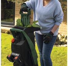Frau bedient einen Akku-Gartenhäcksler von Bosch im Garten.