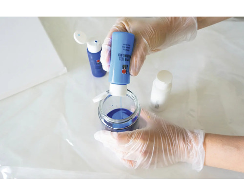 Eine Person mischt blaue Gießharzfarbe in einem Glasbehälter für Kunstprojekte.