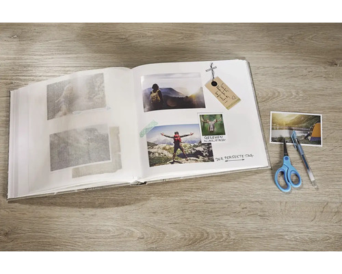 Offenes Fotoalbum mit eingeklebten Bildern, Stift und Schere auf einem Tisch