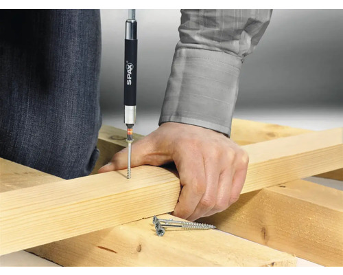 Eine Person schraubt eine Schraube mit einem Schraubendreher in ein Holzbrett. Spax Logo ist sichtbar.