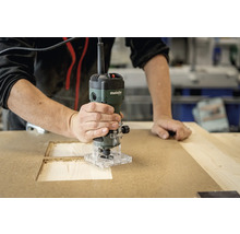 Eine Person benutzt eine Metabo Oberfräse an einem Holzbrett.