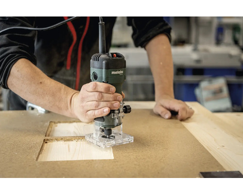 Eine Person benutzt eine Metabo Oberfräse an einem Holzbrett.