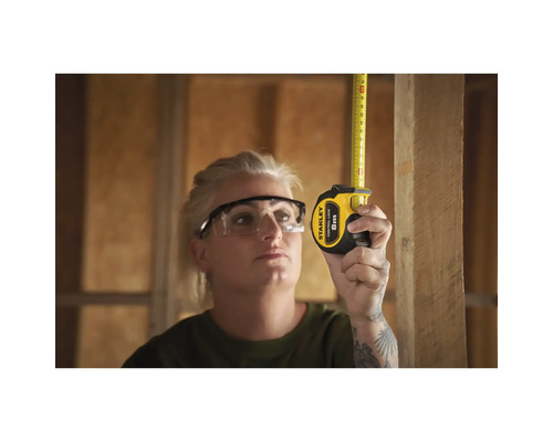 Frau misst mit einem Stanley Rollbandmaß ein Holzbrett