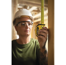 Frau mit Schutzbrille und Bauhelm misst mit einem Stanley Rollbandmaß.