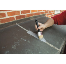 Eine Person trägt mit einem Pinsel eine Abdichtung auf eine Oberfläche auf.