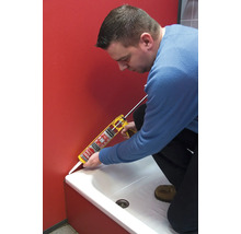 Eine Person dichtet mit einer Kartuschenpistole eine Badewanne ab.