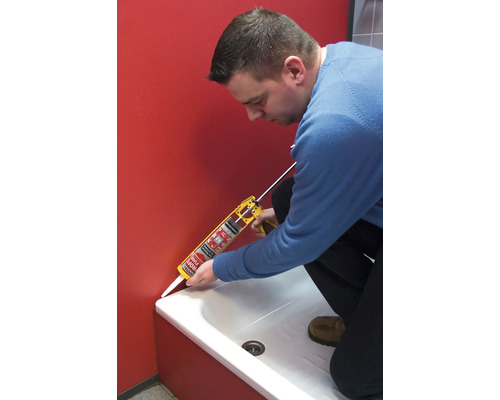 Eine Person dichtet mit einer Kartuschenpistole eine Badewanne ab.