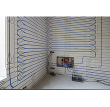 Installation einer Wandheizung mit blauen Rohren auf Paneelen inklusive Heizkreisverteiler.