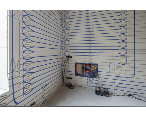 Installation einer Wandheizung mit blauen Rohren auf Paneelen inklusive Heizkreisverteiler.