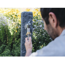Gartenszene mit Wasserhahn an Steinsäule und Person, die einen Schlauch anschließt