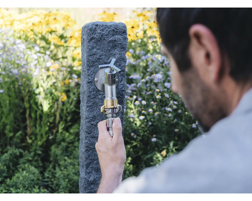 Gartenszene mit Wasserhahn an Steinsäule und Person, die einen Schlauch anschließt