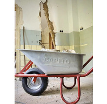 Schubkarre auf einer Baustelle vor einer beschädigten Wand