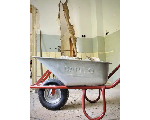 Schubkarre auf einer Baustelle vor einer beschädigten Wand