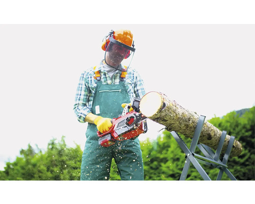 Mann sägt Holz mit einer Kettensäge auf einem Sägebock, er trägt Schutzkleidung