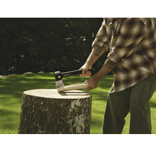 Mann spaltet Holz mit einer Axt auf einem Baumstumpf.