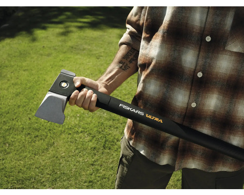 Person hält eine Fiskars Ultra Spaltaxt vor grünem Hintergrund