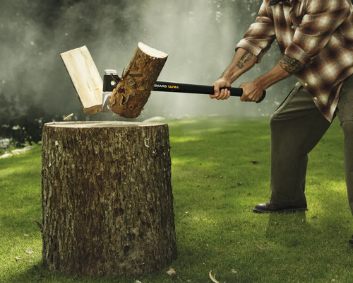 Mann spaltet Holzscheit mit einer Axt auf einem Hackklotz