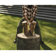 Mann spaltet Holz auf einem Holzscheit mit einer Axt.