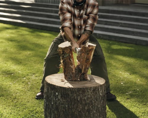 Mann spaltet Holz auf einem Holzscheit mit einer Axt.