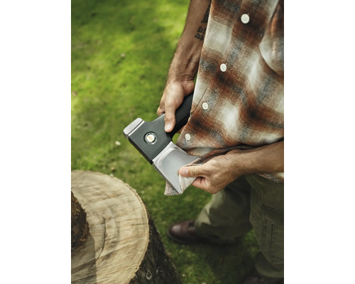 Mann reinigt Axtklinge neben Baumstamm