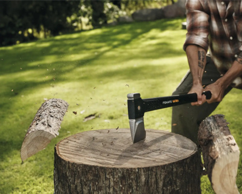 Mann spaltet Holz mit einer Fiskars Axt auf einem Baumstumpf im Freien