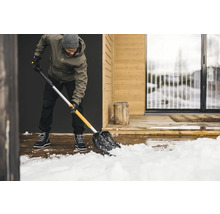 Mann schaufelt Schnee mit einer Schneeschaufel vor einem Haus.
