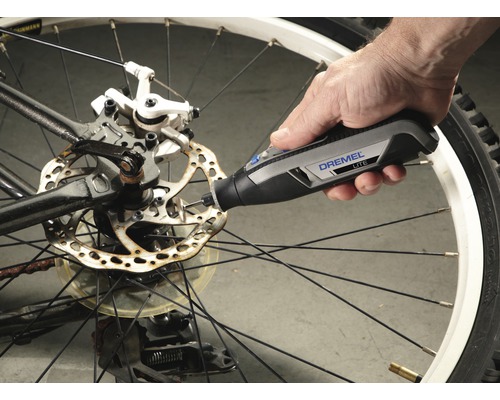 Dremel Logo. Eine Person verwendet ein Dremel Lite Werkzeug an einer Fahrradbremsscheibe.