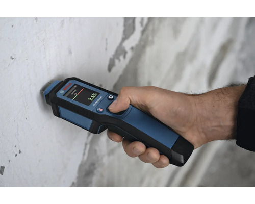 Hand hält ein Feuchtigkeitsmessgerät zur Messung der Wandfeuchtigkeit.