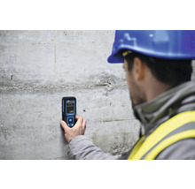 Ein Bauarbeiter misst mit einem Feuchtigkeitsmessgerät die Feuchtigkeit einer Betonwand.