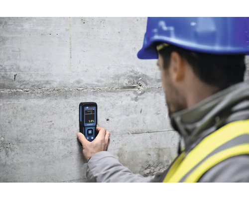 Ein Bauarbeiter misst mit einem Feuchtigkeitsmessgerät die Feuchtigkeit einer Betonwand.