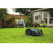 Szene mit Rasenmähroboter auf Rasen und einer Frau, die auf einer Bank sitzt