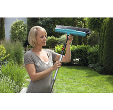 Frau verwendet eine Bürste mit Teleskopstiel im Garten zur Reinigung.