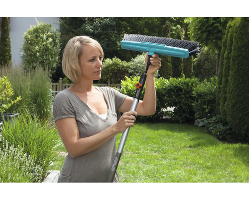 Frau verwendet eine Bürste mit Teleskopstiel im Garten zur Reinigung.