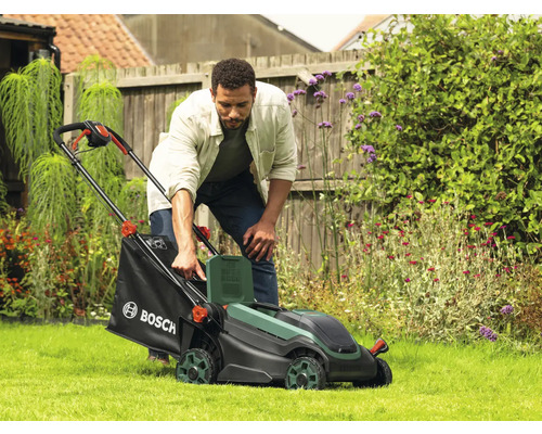 Mann bedient Rasenmäher im Garten. Gartengeräte für die Rasenpflege.