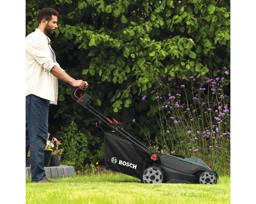 Mann bedient Rasenmäher mit Fangkorb im Garten. Bosch Logo.