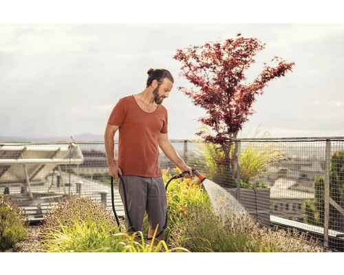 Ein Mann bewässert Pflanzen auf einem Dachgarten mit einem Gartenschlauch.