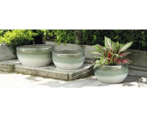 Drei runde Pflanzgefäße aus Keramik auf einer Steinterrasse, eines davon mit einer Pflanze.