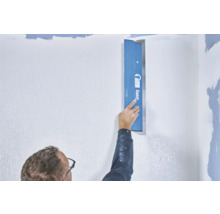 Eine Person glättet eine Wand mit einer Spachtel von Knauf