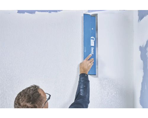 Eine Person glättet eine Wand mit einer Spachtel von Knauf