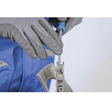 Eine Person feilt mit einer Schlüsselfeile ein Lüftungsgitter, geschützt durch Arbeitshandschuhe.