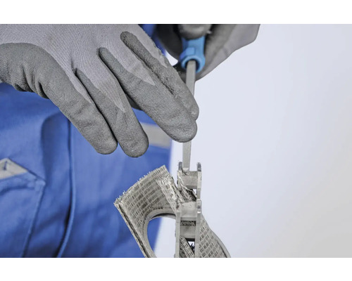 Eine Person feilt mit einer Schlüsselfeile ein Lüftungsgitter, geschützt durch Arbeitshandschuhe.