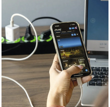 Eine Person bedient eine Smartphone App mit dem Shelly Logo, im Hintergrund eine Steckdosenleiste und ein Laptop