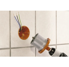 Eine Bohrmaschine mit einer Lochsäge bohrt ein Loch in eine geflieste Wand für eine Steckdose.