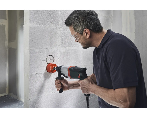 Mann bohrt mit einer Lochsäge ein Loch in eine Wand.